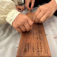 Children playing with a wooden travel size Cribbage board on a textured surface
