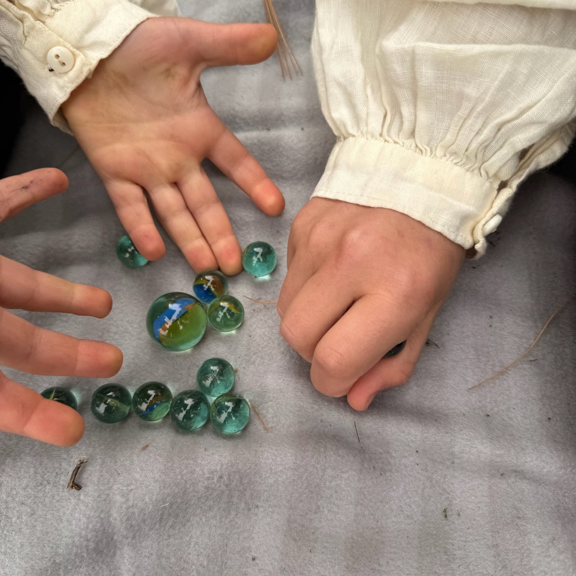 Children's hands playing with marbles on a gray surface