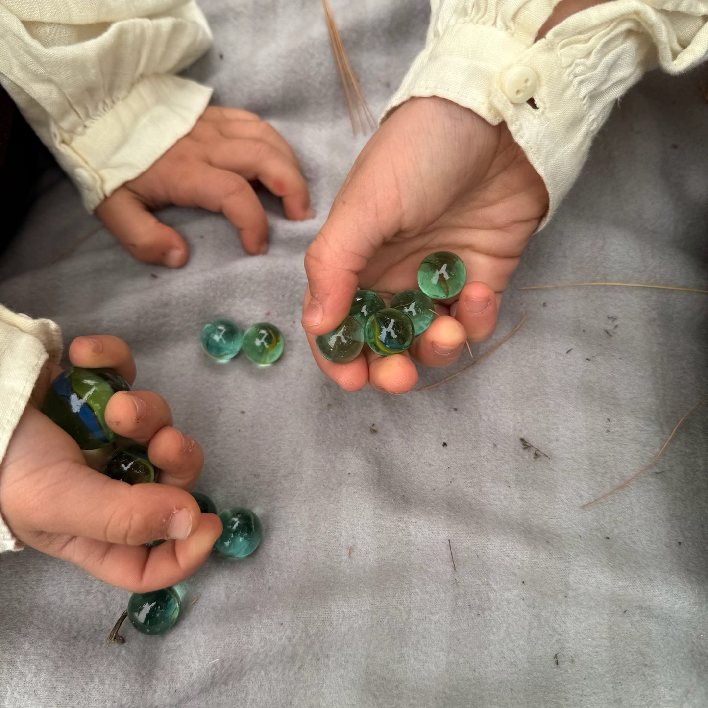 Children's hands holding green marbles on a textured surface