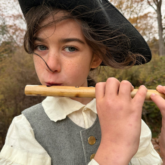 Child playing a bamboo fife outdoors with trees in the background
