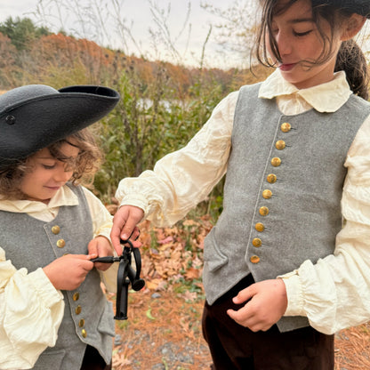 Two children holding black iron shackles in colonial attire standing outdoors with trees in the background.