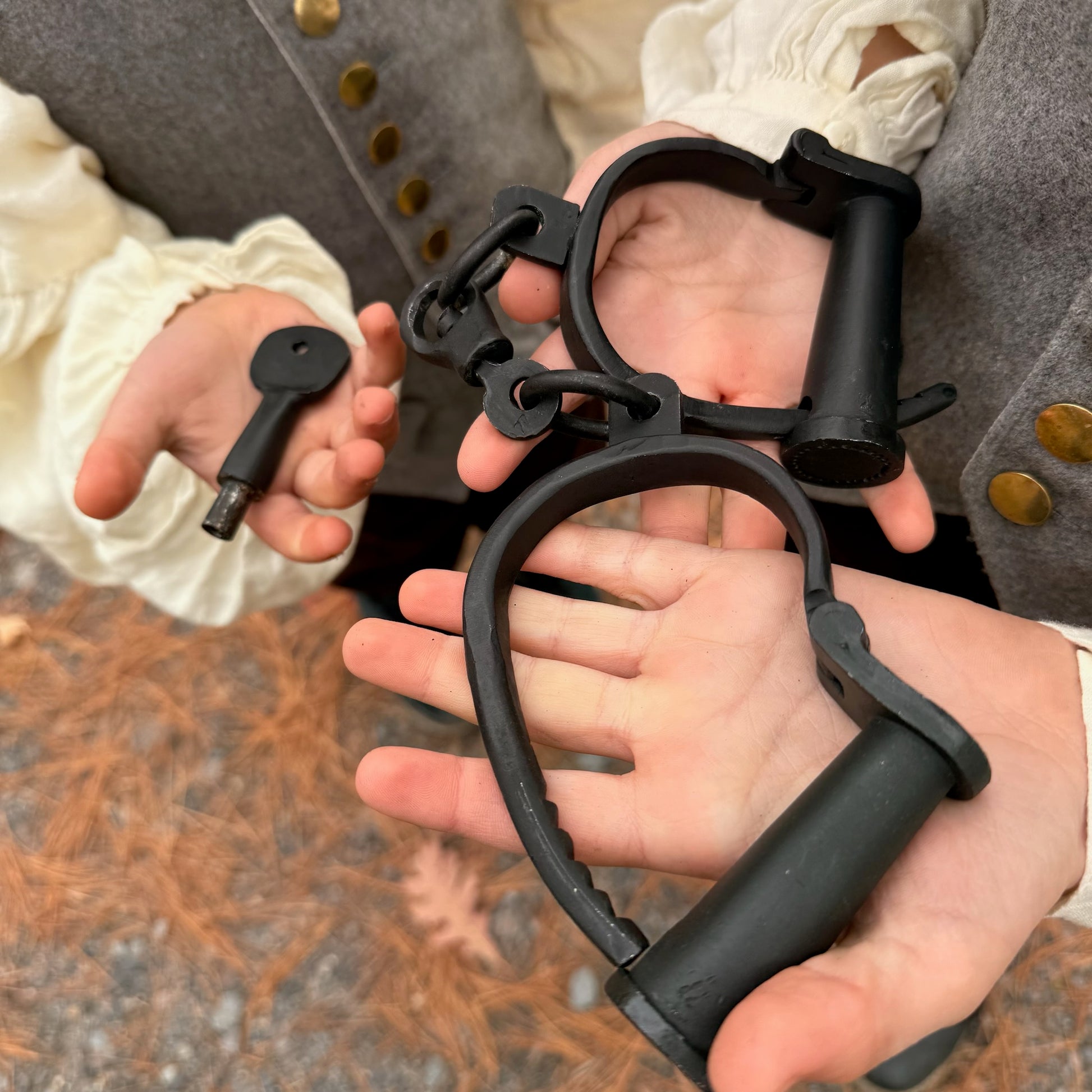 Black iron shackles held by hands with a blurred background