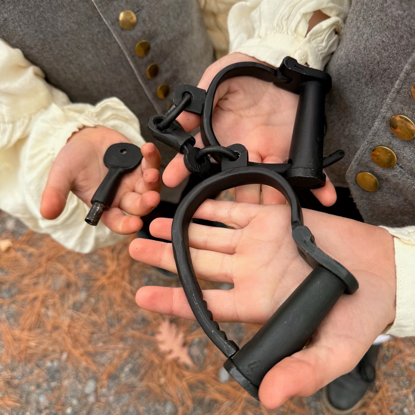 Children wearing colonial style clothing holding black iron shackles with a key.