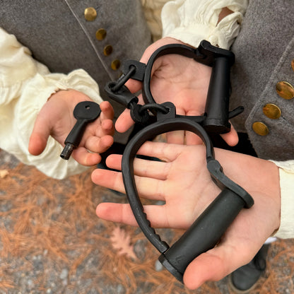 Children wearing colonial style clothing holding black iron shackles with a key.