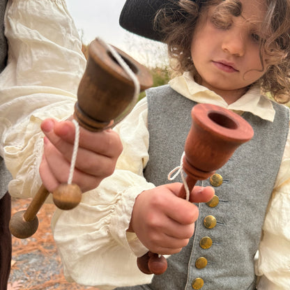 Children in historical attire holding cup and ball toys outdoors