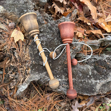 Two wooden cup and ball toys on a rocky surface with leaves