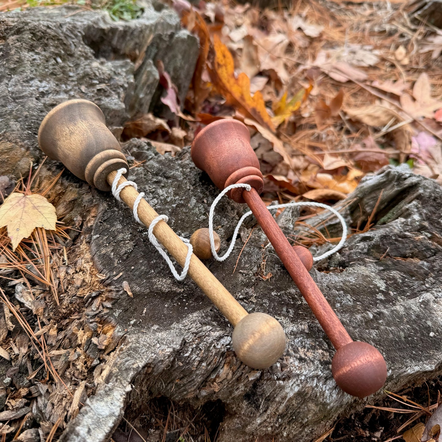 Two wooden cup and ball toys on a stone surface with leaves and twigs in the background