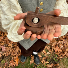 Child holding a wooden drop top toy outdoors with leaves on the ground