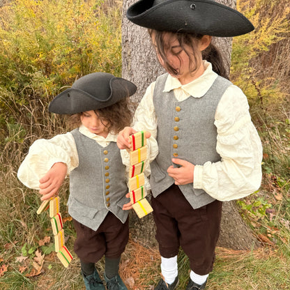 Two children in colonial-style clothing standing outdoors near a tree playing with Jacob's Ladder toys.