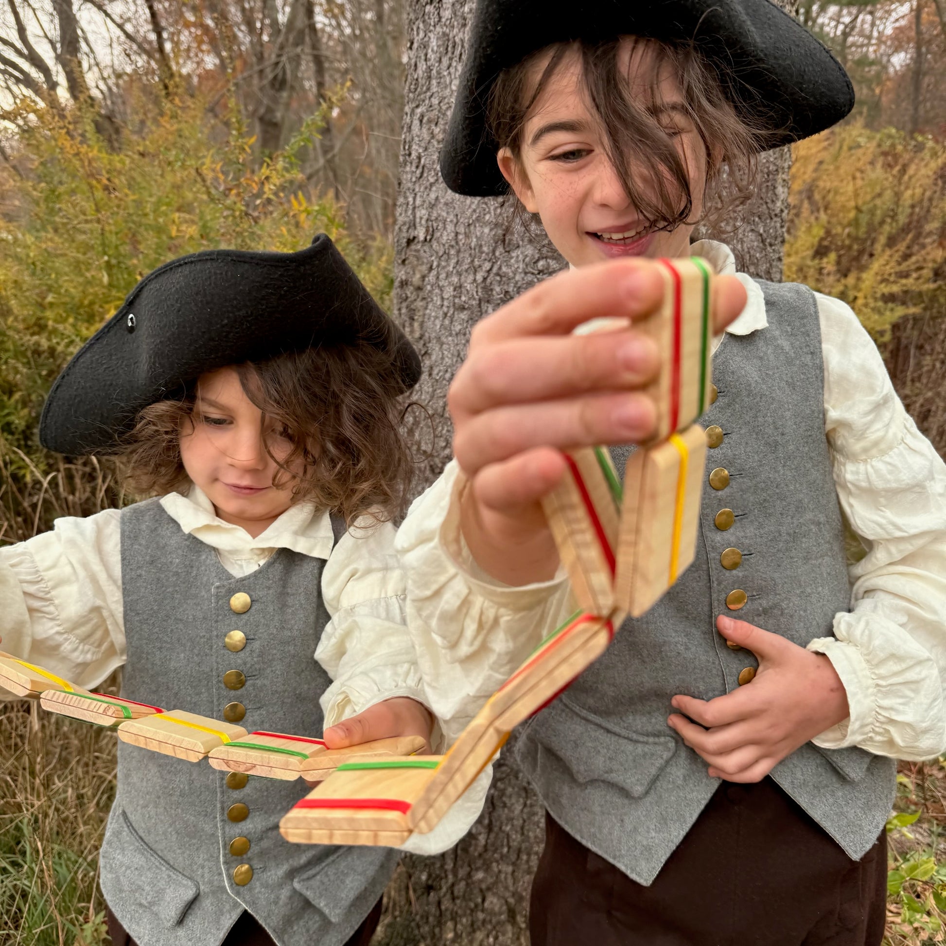 Two children in colonial attire playing with Jacob's Ladder toys outdoors.