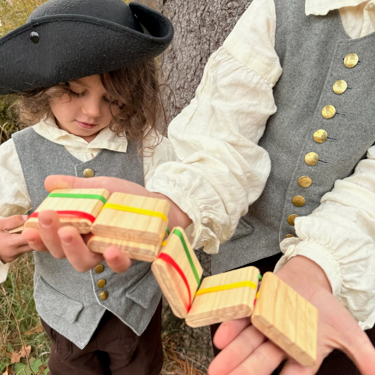 Two children in colonial attire playing with Jacob's Ladder toys outdoors.
