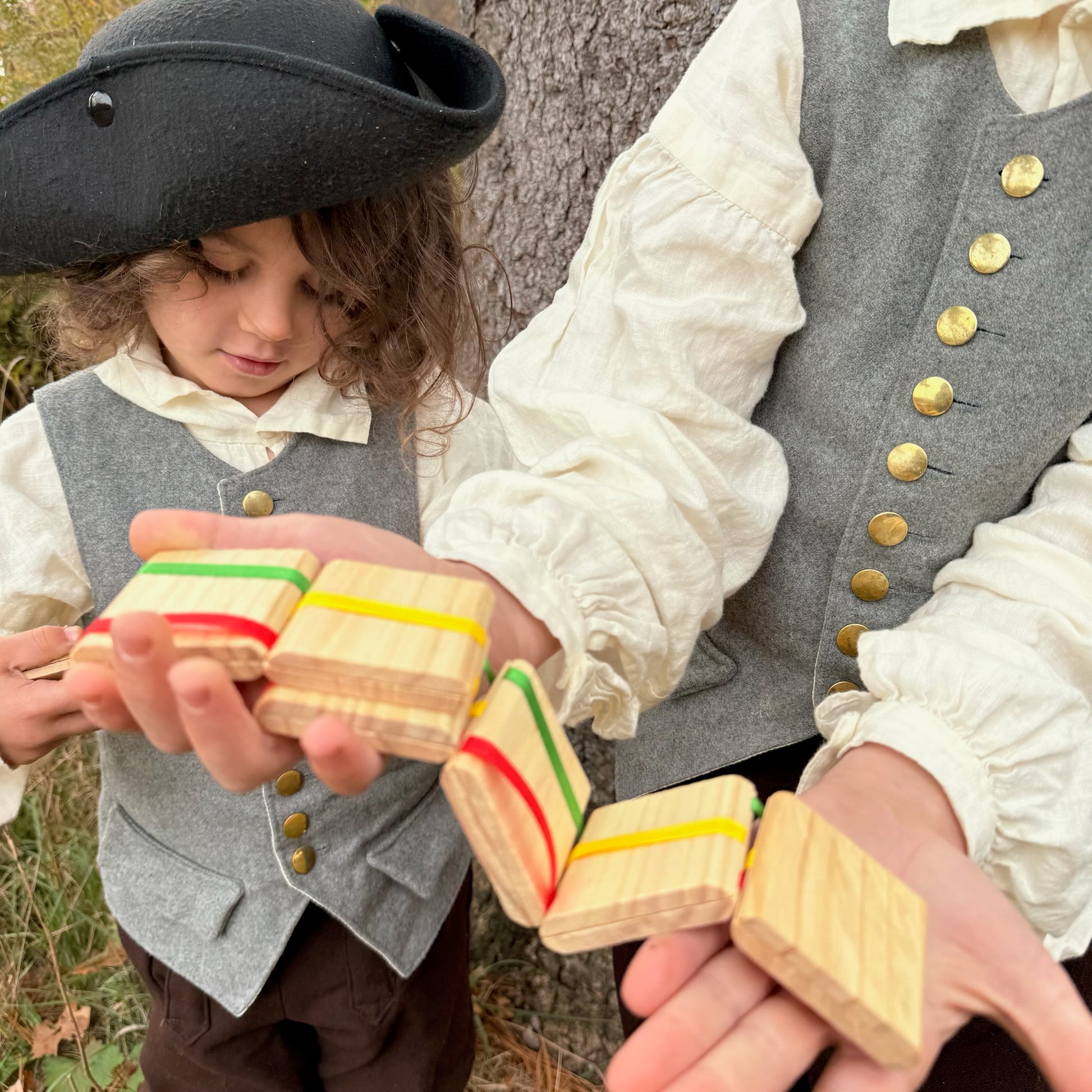 Two children in colonial attire playing with Jacob's Ladder toys outdoors.