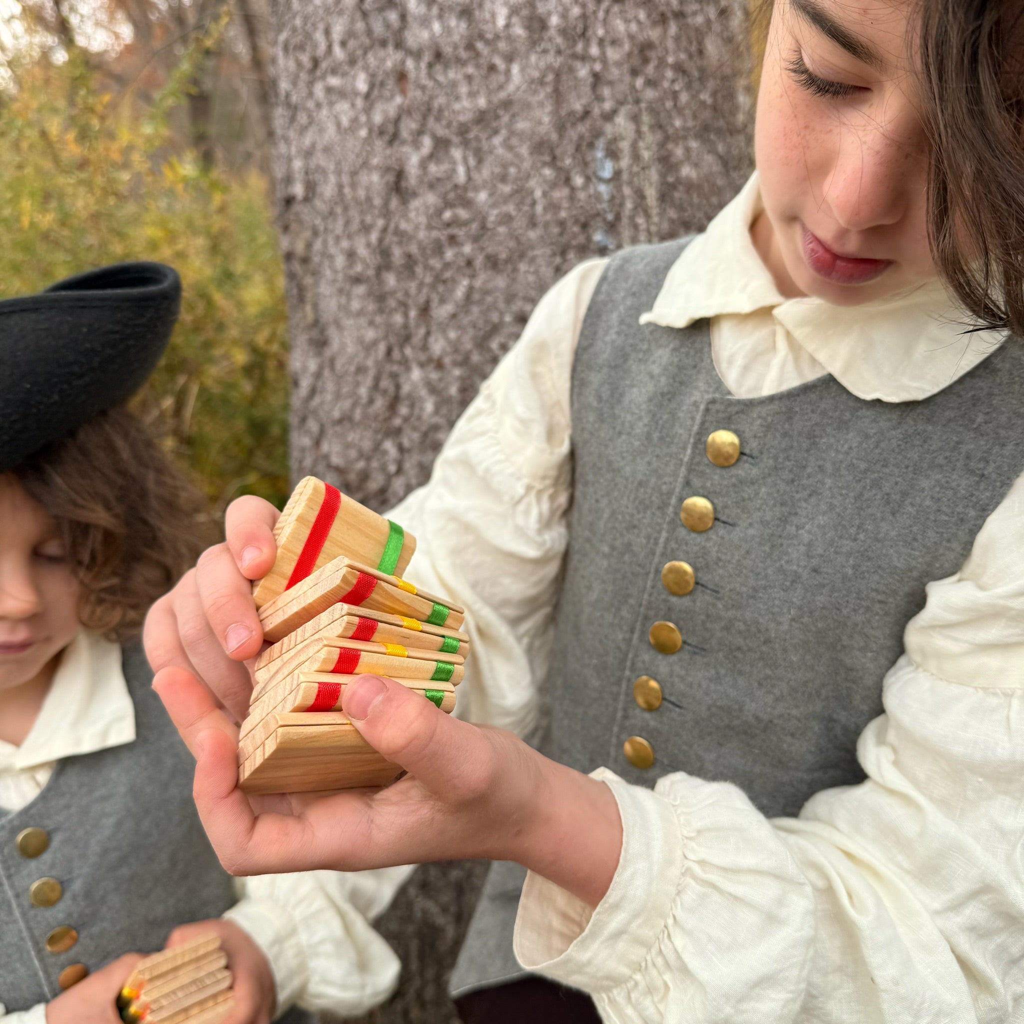 Two children in colonial attire playing with Jacob's Ladder toys outdoors.