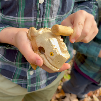 Child holding a wooden Croaky Frog toy, wearing a plaid shirt.